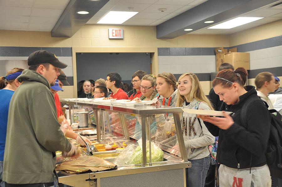 Students wait in line to get their food while vendors on the right provide assistance.  
