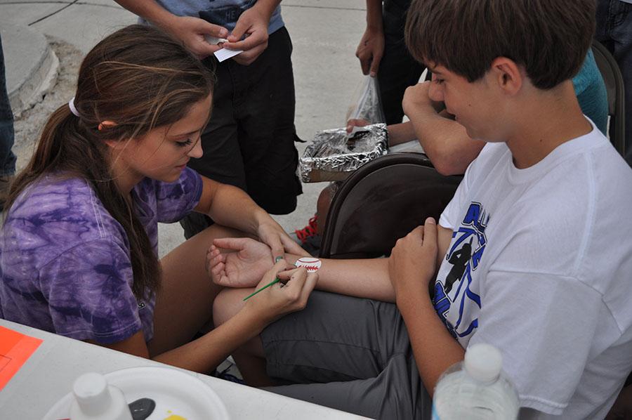 Shae Toof paints a young boys arm at the basketball face painting stand. 